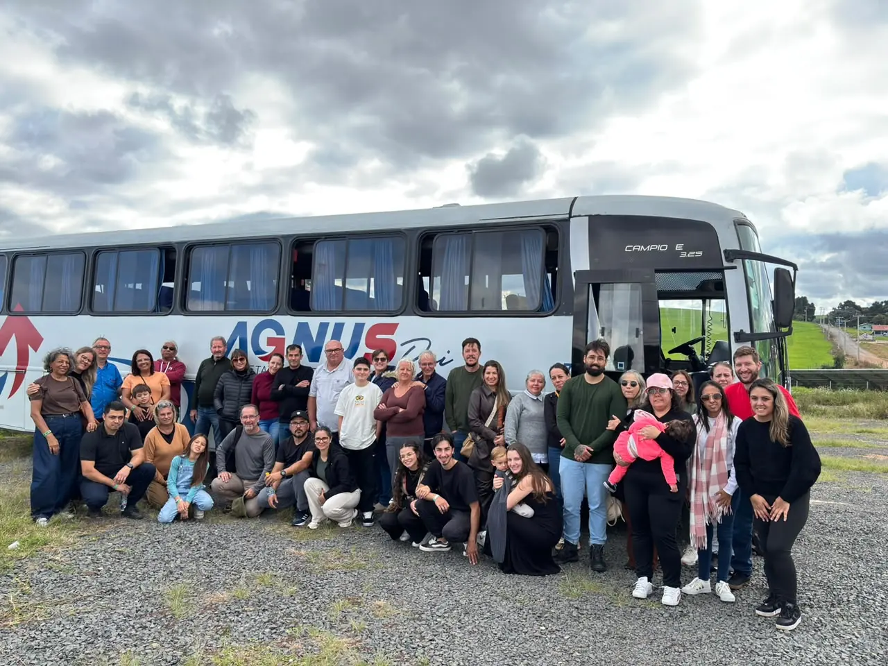 Grupo de passageiros reunido em frente a um ônibus da Agnus durante uma viagem.